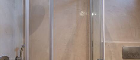 A modern shower with a glass enclosure, a handheld showerhead, and a handheld faucet.