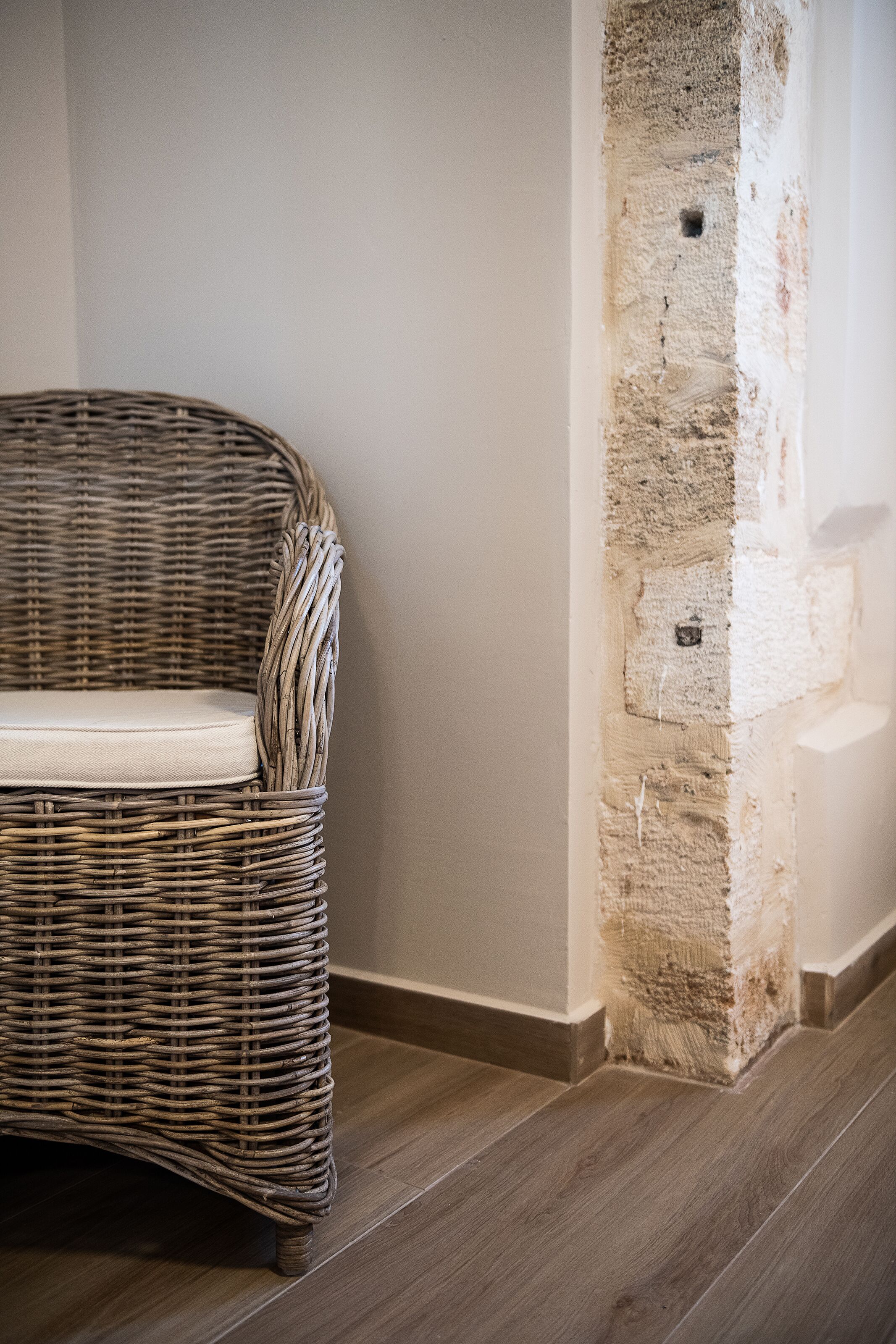 A wicker chair with a cushion against a wall with exposed brickwork.