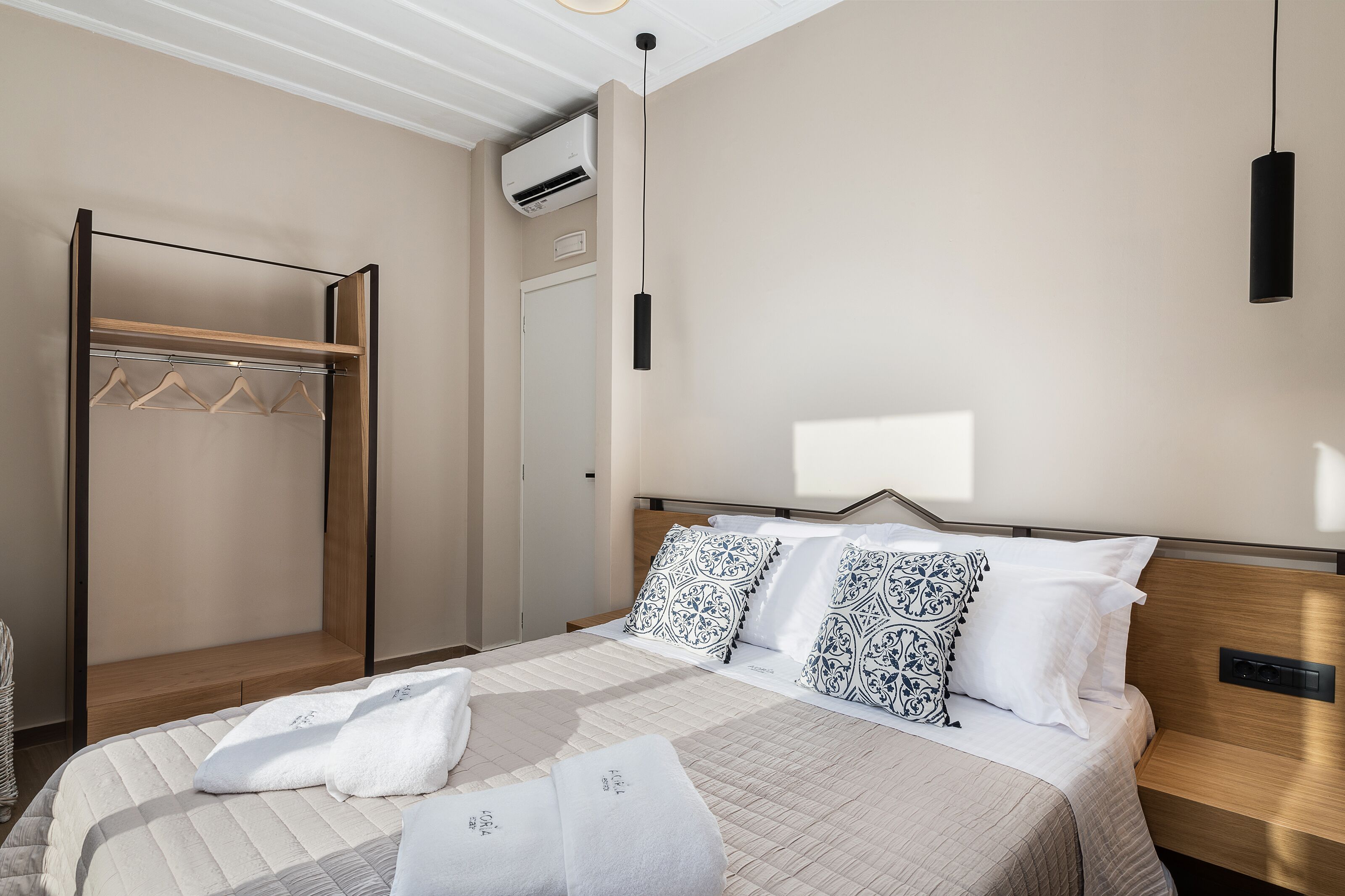 A hotel room with a bed, a wooden bench, a wardrobe, and a hanging light fixture.