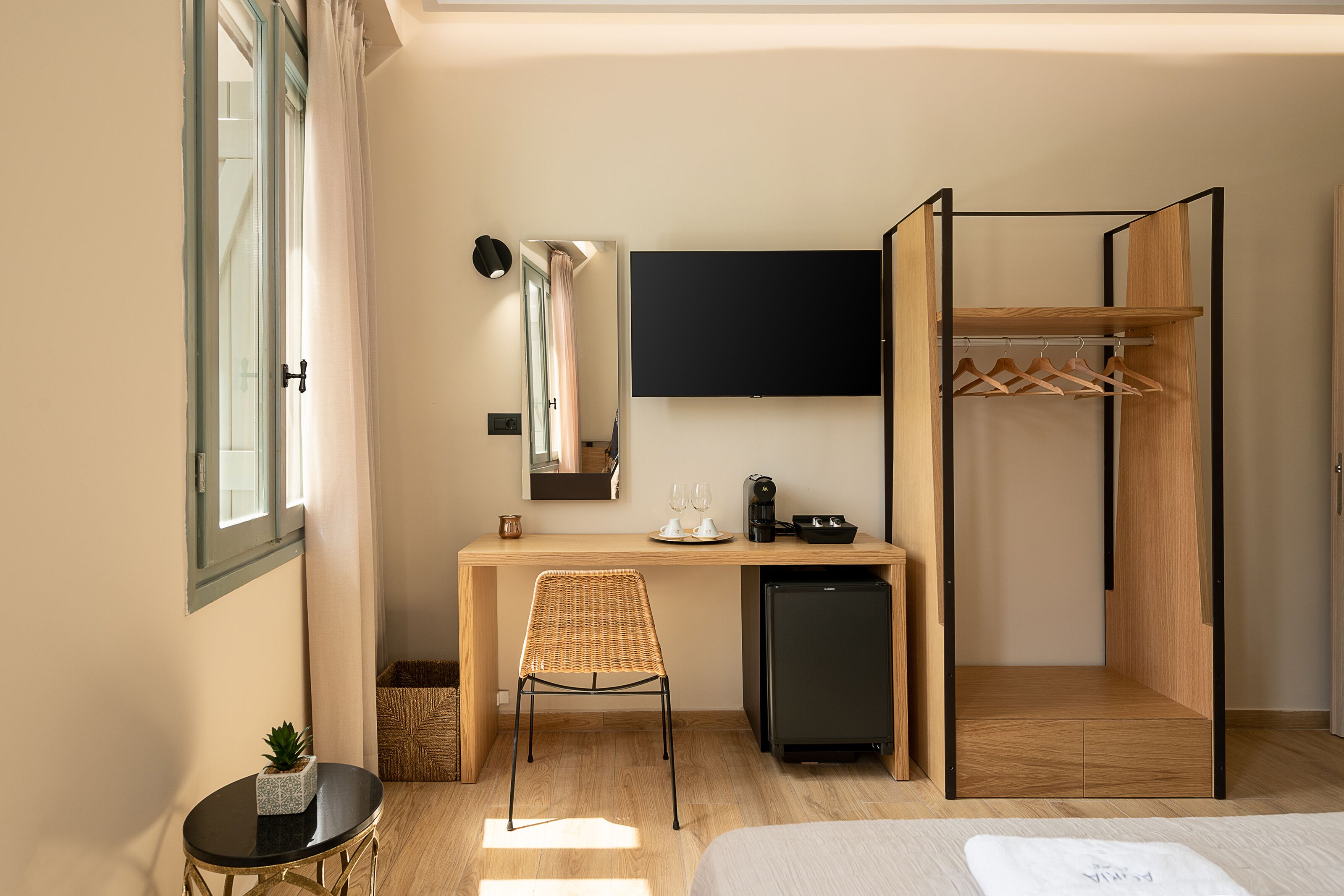 Una habitación de hotel compacta con una cama, un escritorio con ordenador, un refrigerador pequeño, una silla y un armario.