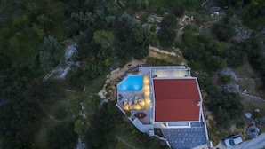 Una vista aerea di una casa con piscina, tetto rosso e patio con posti a sedere.