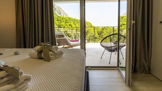 Una camera d'albergo con un letto, un balcone con una sedia e vista sul verde.