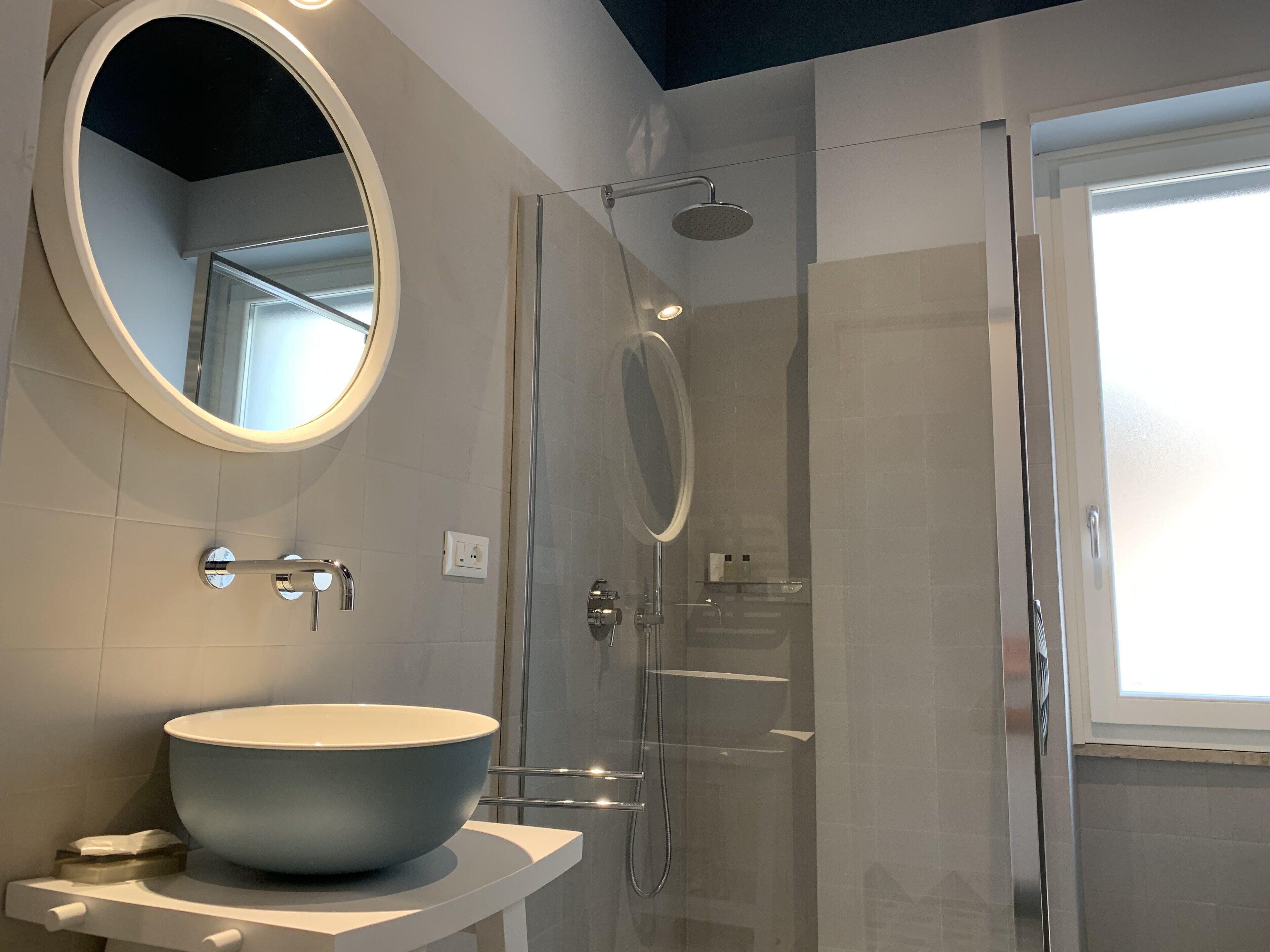 A modern bathroom with a large oval sink, a glass-enclosed shower, and a round mirror.