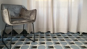 A room with a modern chair, a patterned floor, and sheer curtains. - UNICO - Art & Decor (Ostuni)