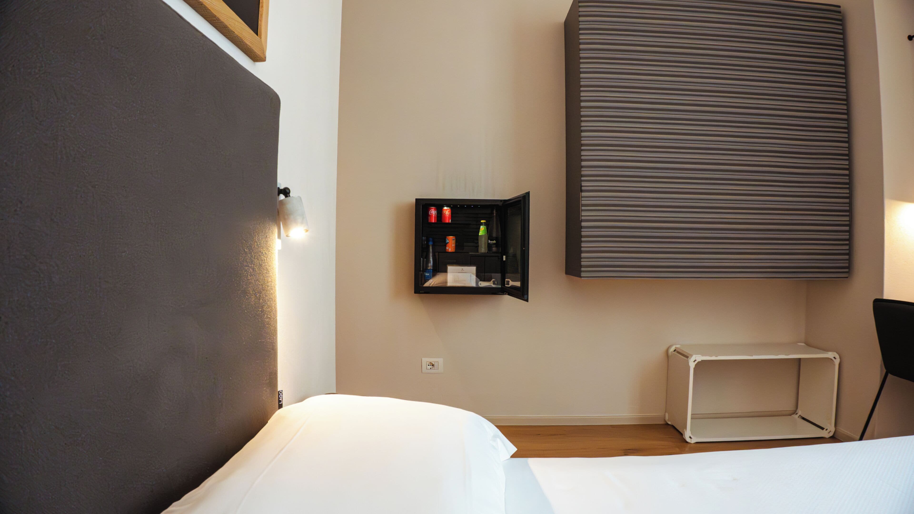 Habitación de hotel con cama, un mueble pequeño con artículos de aseo, radiador fijado a la pared y una pared lisa.