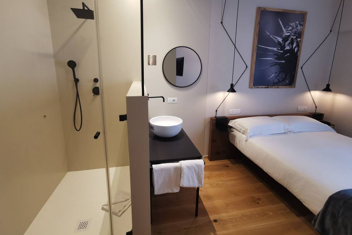 A modern bedroom with a bed, bedside table, and a small bathroom with a sink and shower.