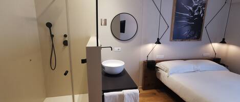 A modern bedroom with a bed, bedside table, and a small bathroom with a sink and shower.