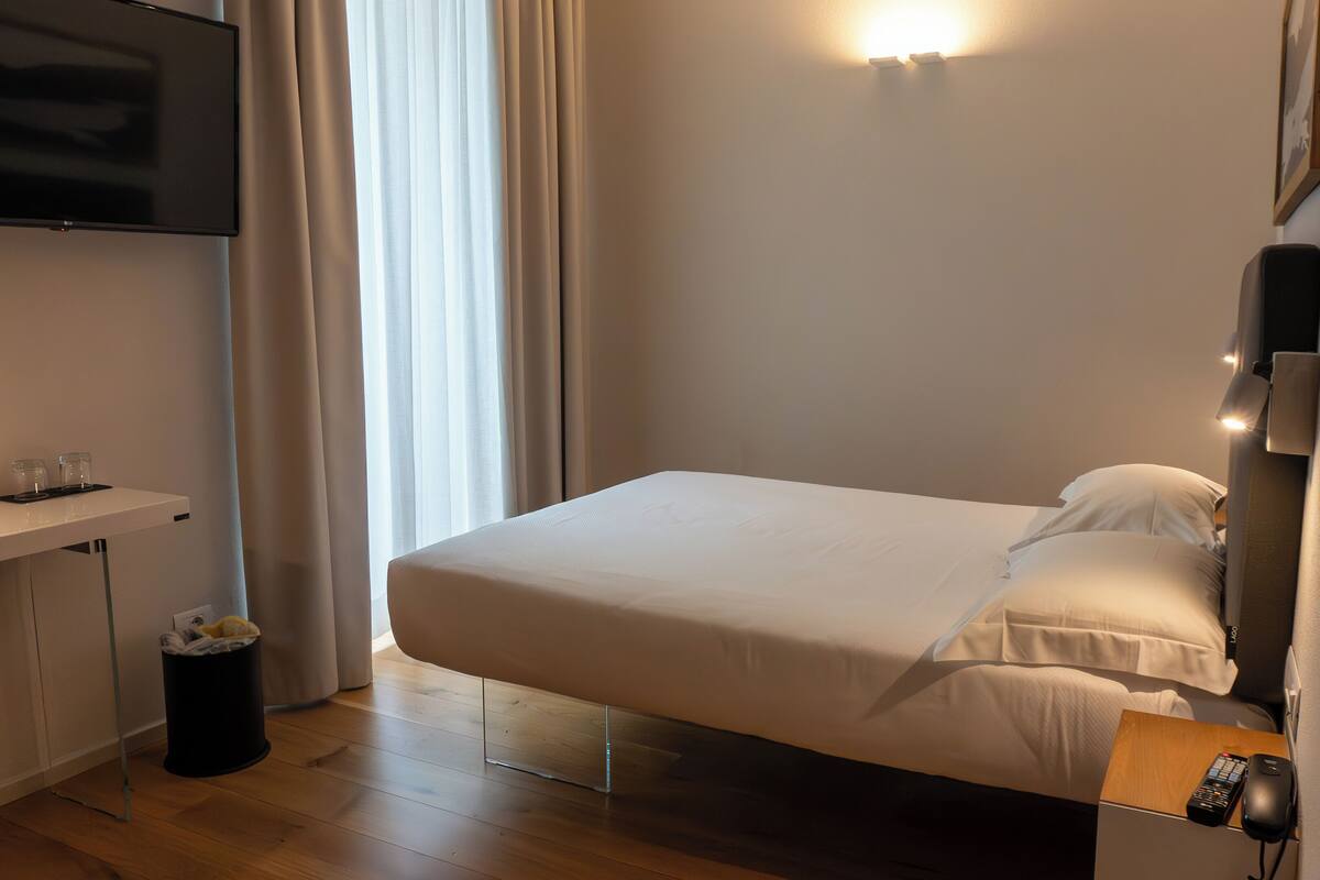 A neatly arranged hotel room with a bed, a desk, a TV, and a trash bin.