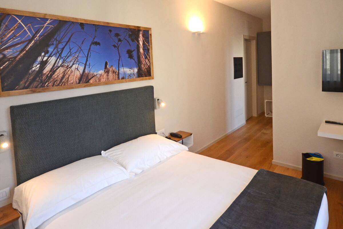 A hotel room with a bed, a painting, a TV, and a desk.