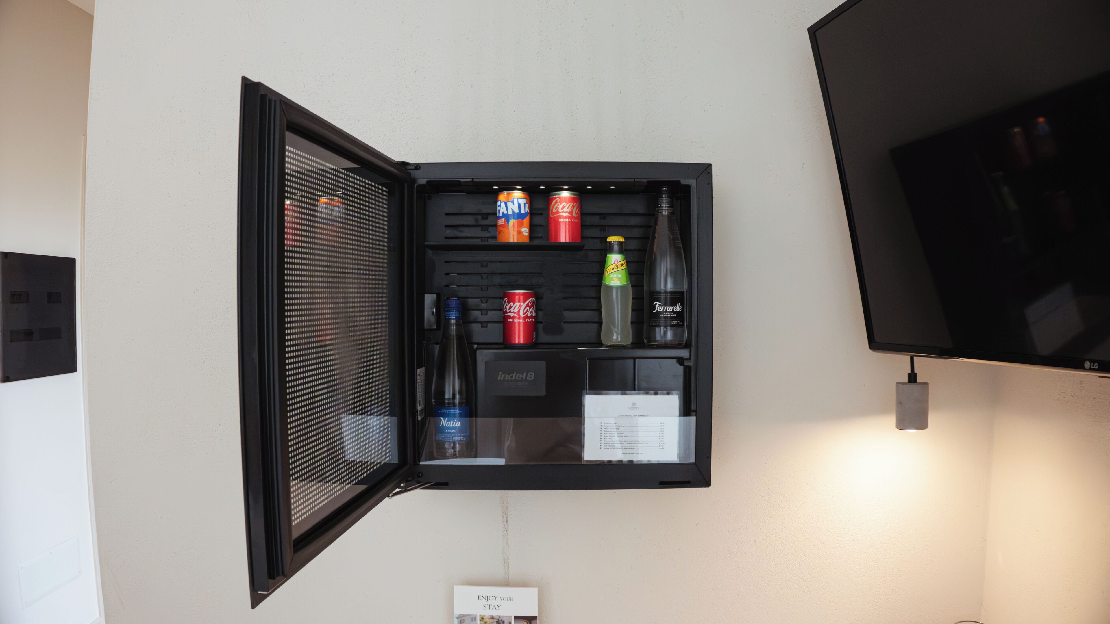 Un minibar con diversas bebidas y un televisor fijado en la pared.