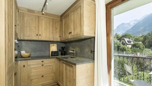 Eine kleine Küche mit Holzausstattung und Blick auf eine gebirgige Landschaft vom Balkon aus.