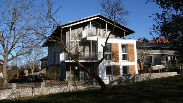 A modern two-story house with a balcony, a stone wall, and a car parked in the driveway. - Apartment 1 with mountain view (Söllhuben)