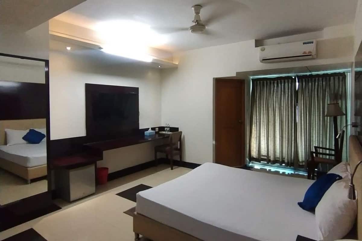 A hotel room with a bed, a desk, a TV, and an air conditioning unit.