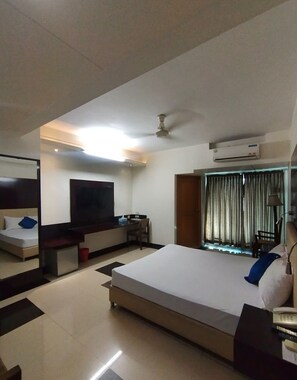 A hotel room with a bed, a desk, a TV, and an air conditioning unit.