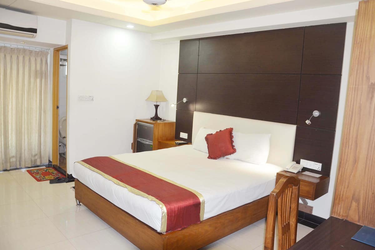 A hotel room with a large bed, a wooden nightstand, a desk, and a chair.