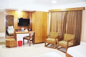 A hotel room with a wooden wardrobe, a desk with a chair, a television, and a large window with curtains.