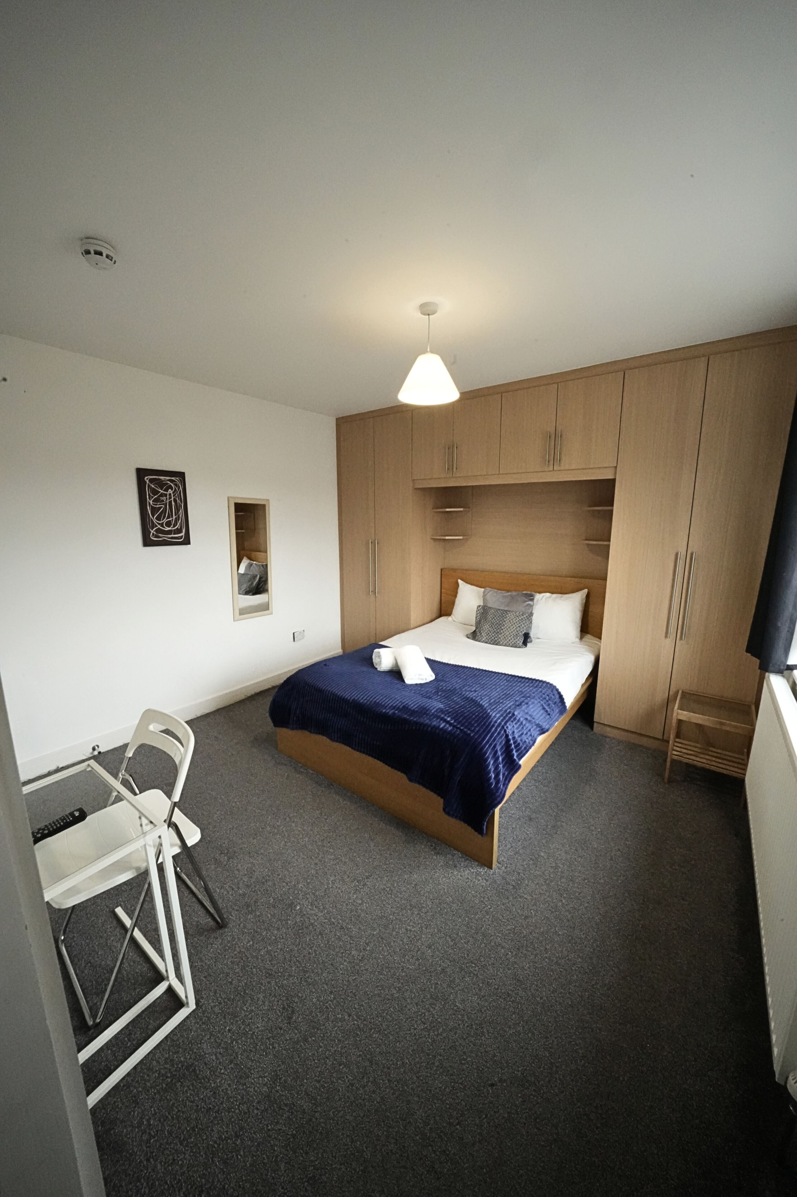 A bedroom with a bed, a desk, a chair, and a wardrobe.