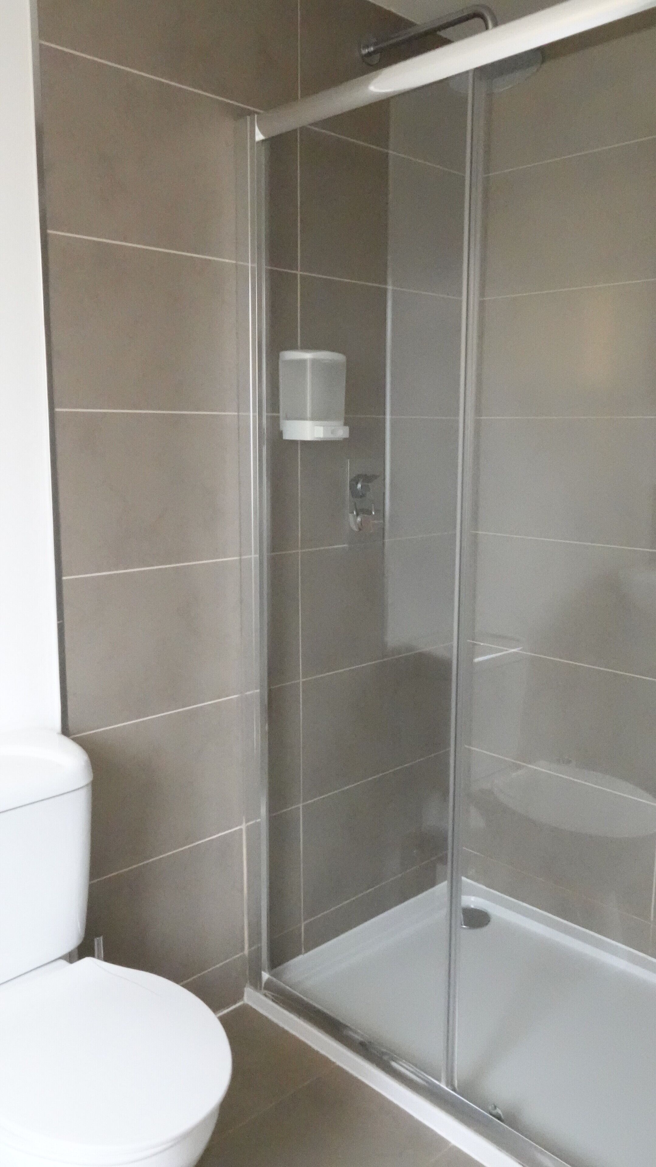 Un baño moderno con ducha de vidrio, inodoro y dispensador de jabón en la pared.