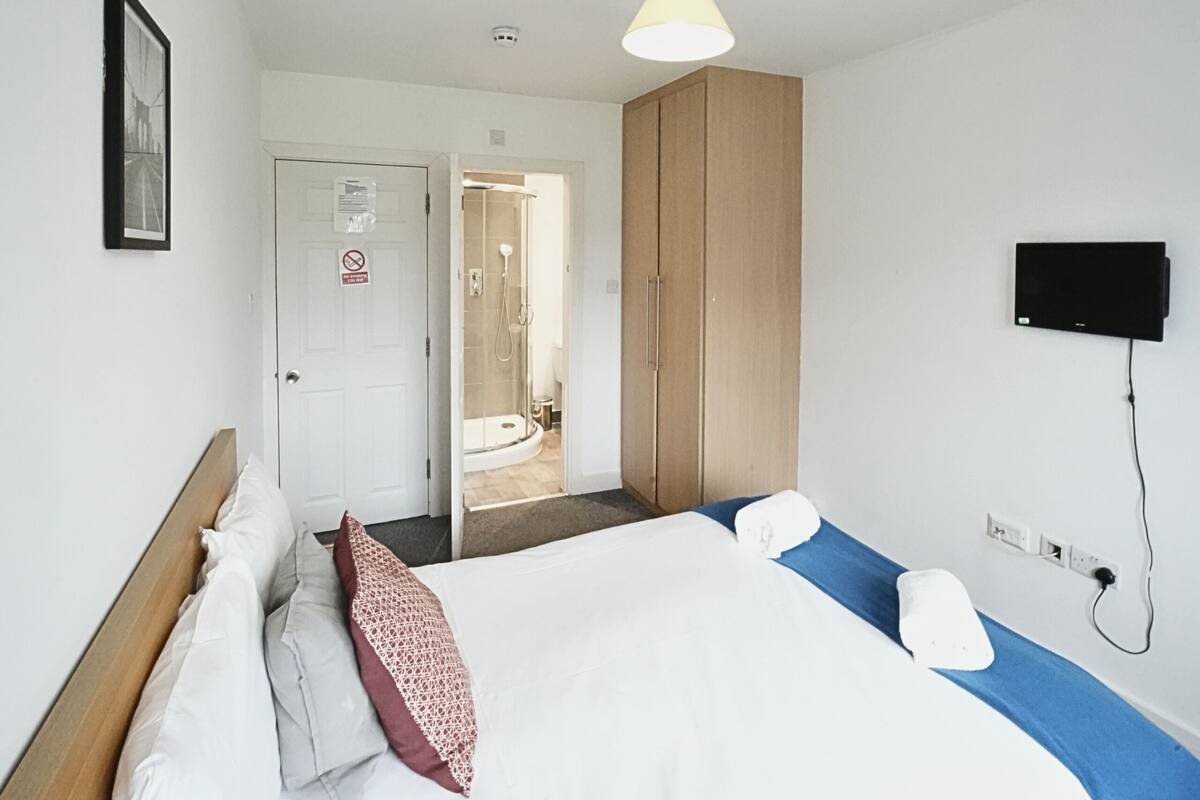 Ein Hotelzimmer mit Bett, Kleiderschrank, Duschbereich und einem an der Wand montierten Fernseher.
