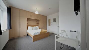 A bedroom with a bed, a desk, and a wardrobe.