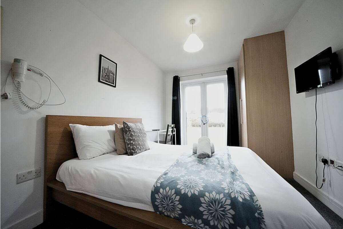 Ein ordentlich bezogenes Bett mit floraler Decke, ein an der Wand montierter Fernseher und ein Fön.