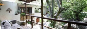 A covered outdoor seating area with a wooden deck, a sofa, and a railing. - Little Forest Guest House (Randburg)