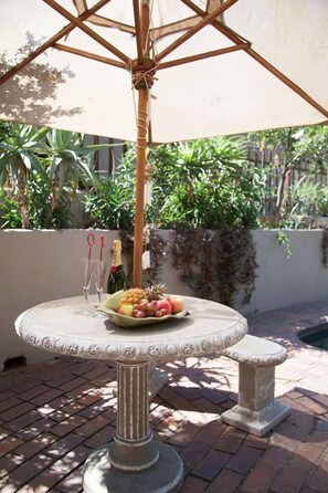 A table with a decorative umbrella, a bottle of champagne, and a fruit plate. - Little Forest Guest House (Randburg)