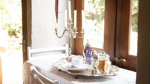 Une table à manger recouverte d’une nappe blanche, un service à thé, un bocal en verre contenant du pain et un chandelier avec des bougies.