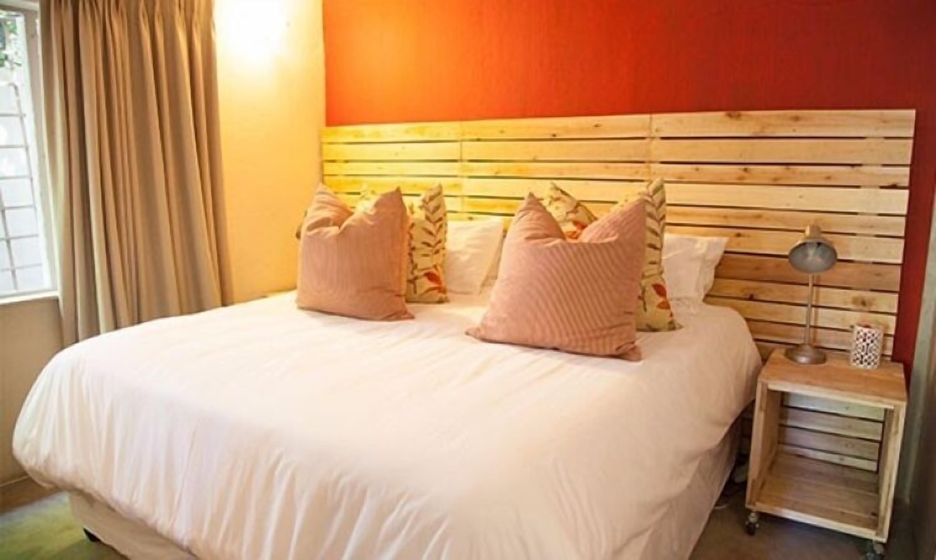 Quarto com cabeceira de madeira, colcha branca e várias almofadas.