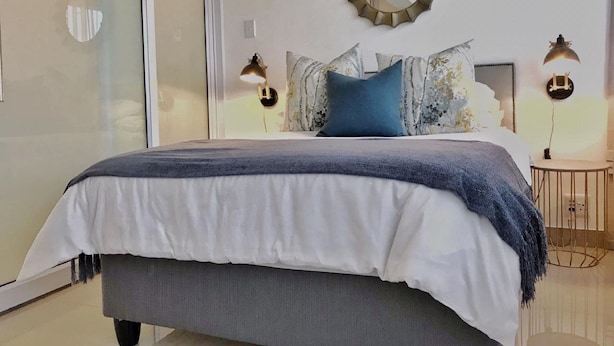 Un dormitorio moderno con una cama grande, un espejo redondo y dos lámparas de noche.