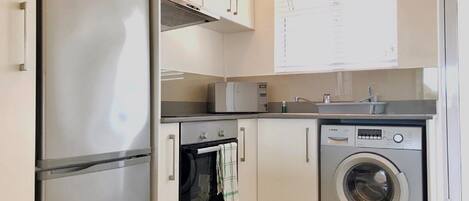 Cocina compacta equipada con refrigerador, horno, microondas y lavadora.