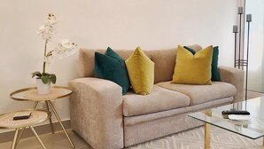 Una sala de estar con un sofá color beige, una mesita redonda con una planta y una mesa de centro de vidrio.
