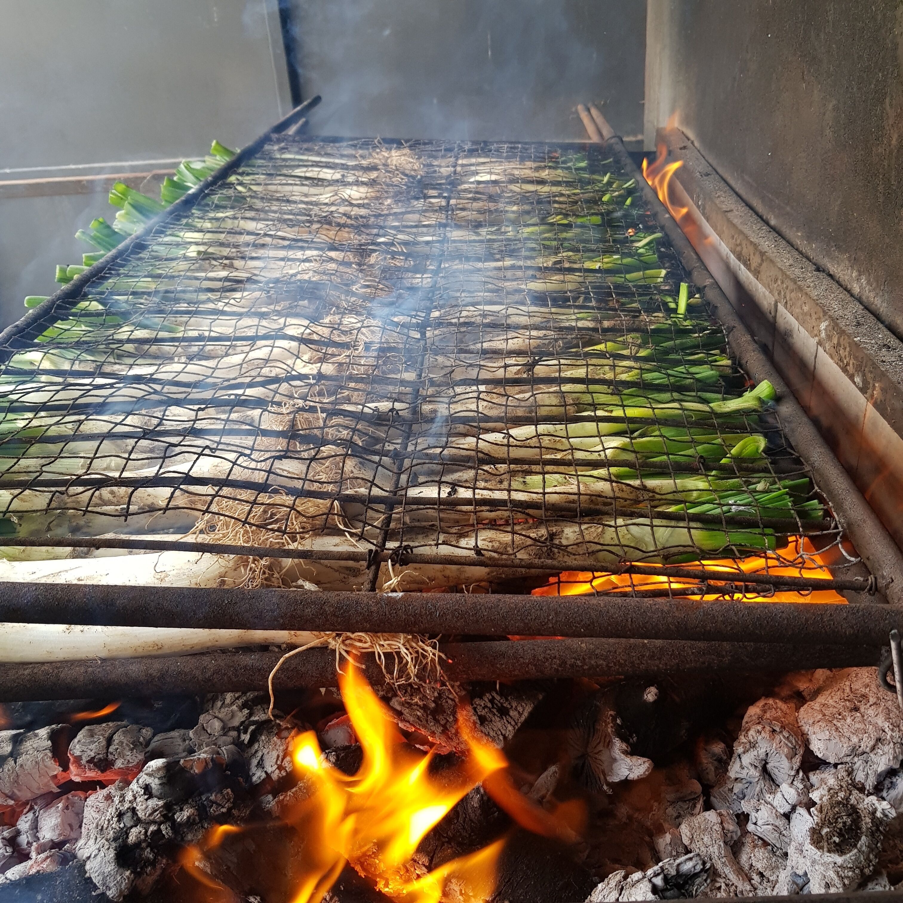 Una parrilla con vegetales verdes cocinándose sobre fuego abierto.