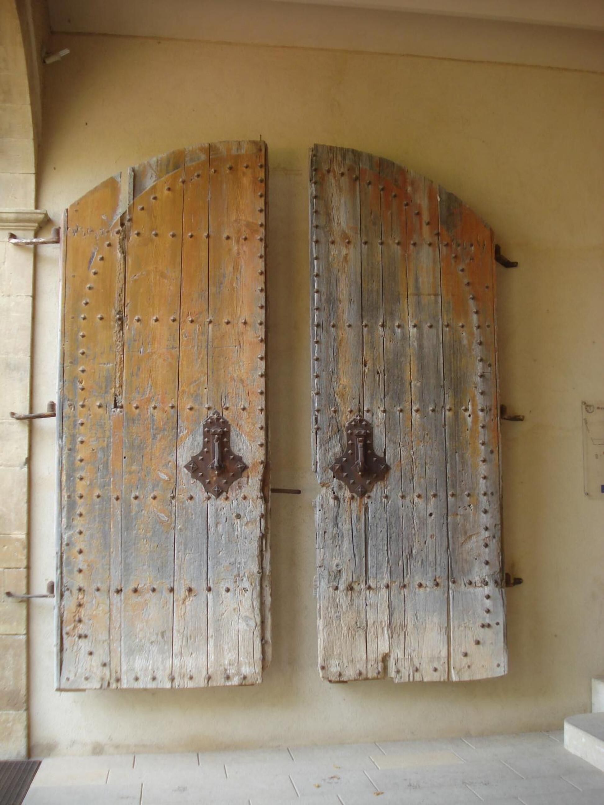 A pair of large, weathered wooden doors with metal studs and decorative metal hinges.