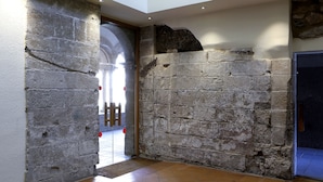 Un mur de pierre à la texture rugueuse, avec une porte donnant sur un espace plus lumineux.