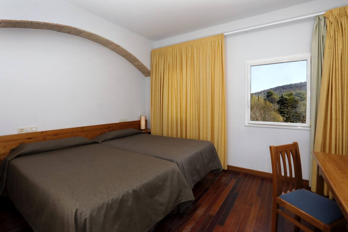 Een kamer met twee bedden, een houten bureau, een stoel en een raam met gordijnen.