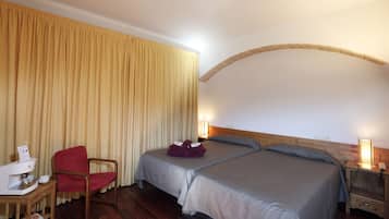 Habitación de hotel con dos camas, una silla de madera, una mesita de noche con lámpara y una cortina.