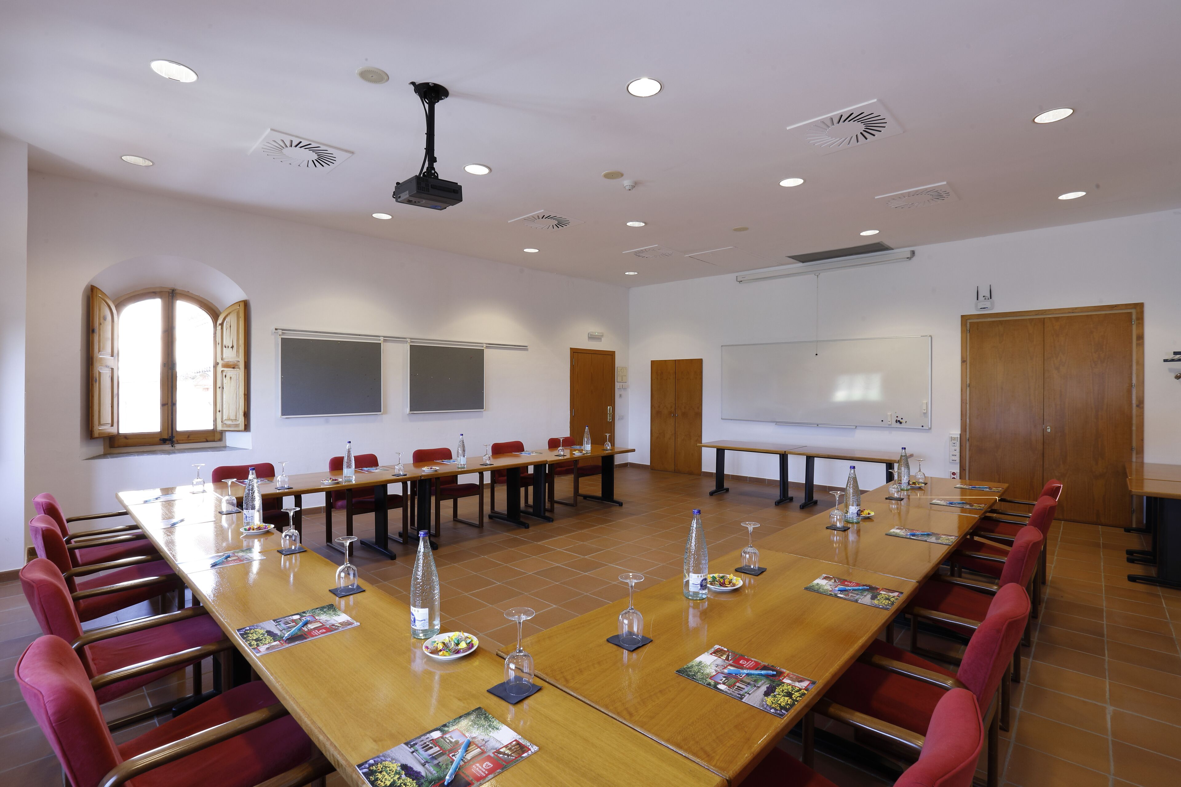 A conference room with a long table, red chairs, water bottles, and a whiteboard.