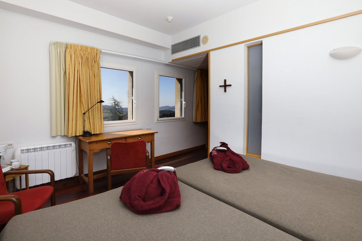 Een hotelkamer met twee eenpersoonsbedden, een bureau, een stoel, een raam met gordijnen en een radiator.