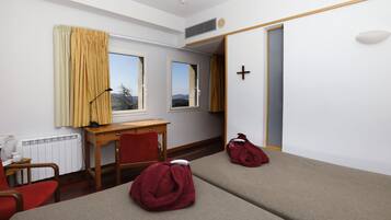 Habitación de hotel con dos camas individuales, un escritorio, una silla, una ventana con cortinas y un radiador.