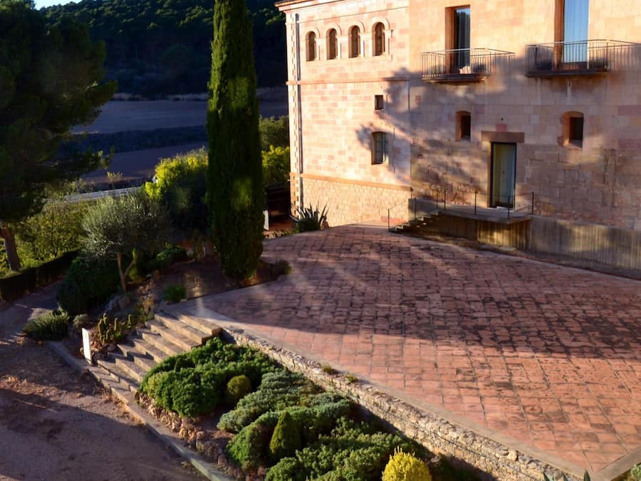 A stone building with a paved driveway and a garden with various shrubs.