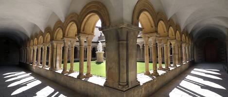 A corridor with a series of arches and columns, leading to a courtyard with a statue.