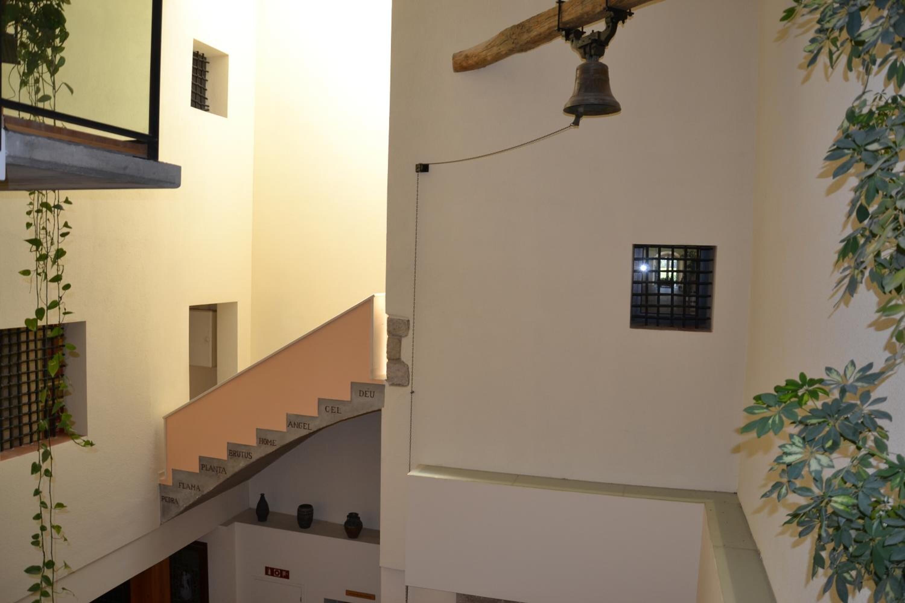 Eine Treppe mit Stufen, die mit Zimmernamen beschriftet sind, eine hängende Glocke und ein kleines Fenster mit Gitterstäben.