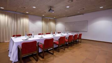 Un salón de conferencias con una larga mesa, sillas rojas, un proyector y una pizarra.