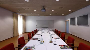 Ein Konferenzraum mit langem Tisch, roten Stühlen, einem Projektor und einer Whiteboard-Tafel.