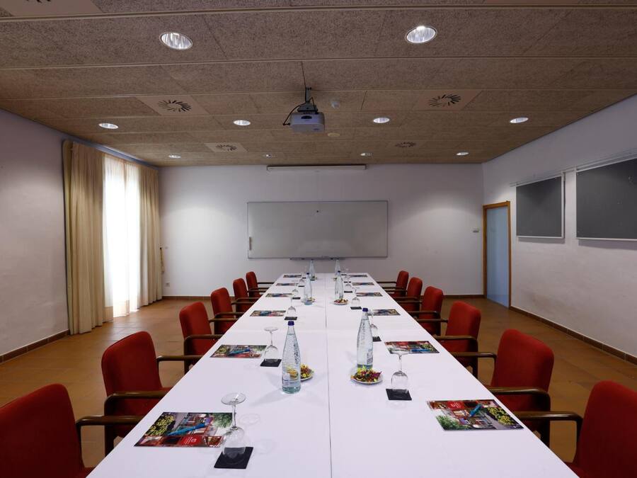 Ein Konferenzraum mit langem Tisch, roten Stühlen, einem Projektor und einer Whiteboard-Tafel.