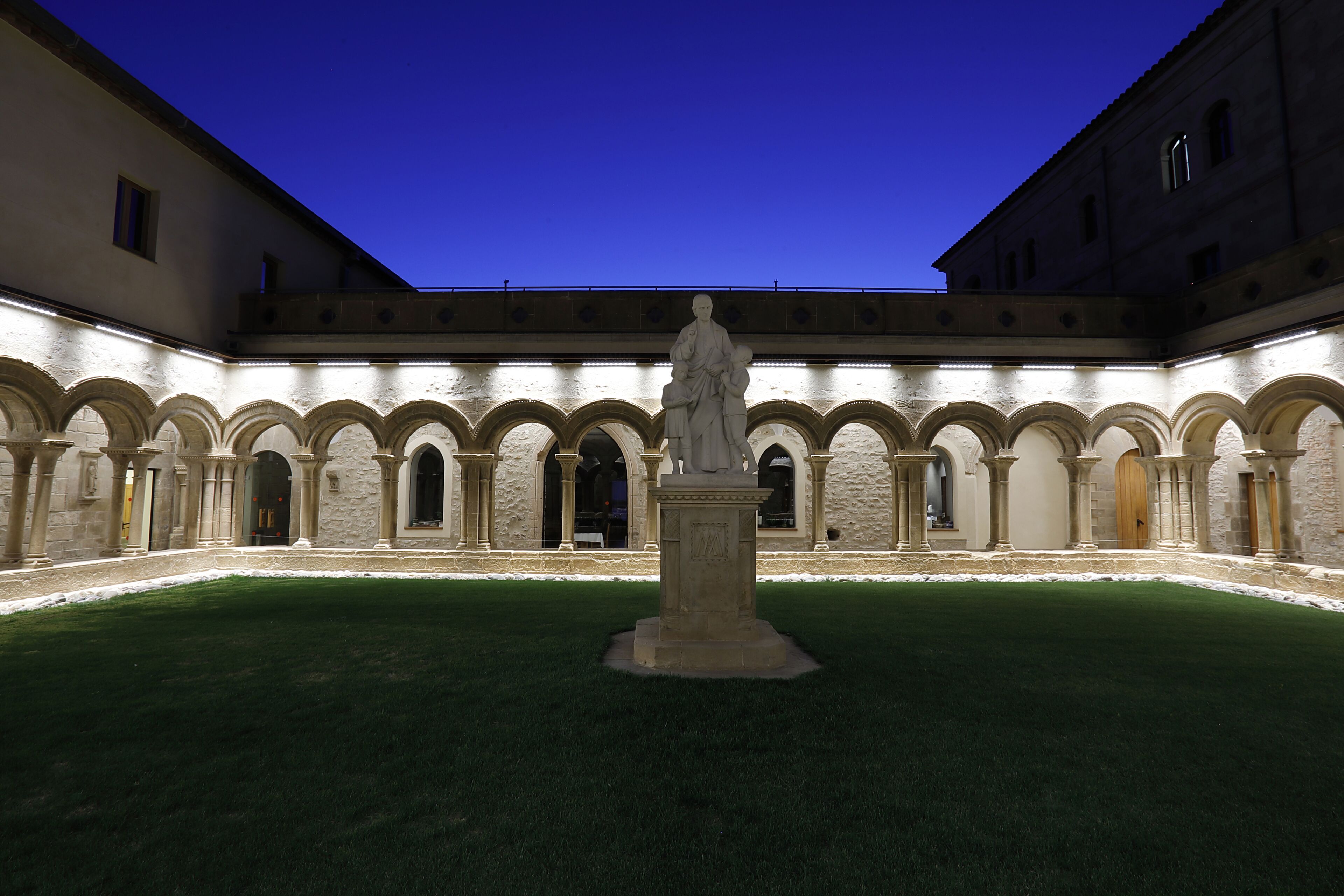 Une cour intérieure avec une statue au centre, entourée d’arcades et de bâtiments.
