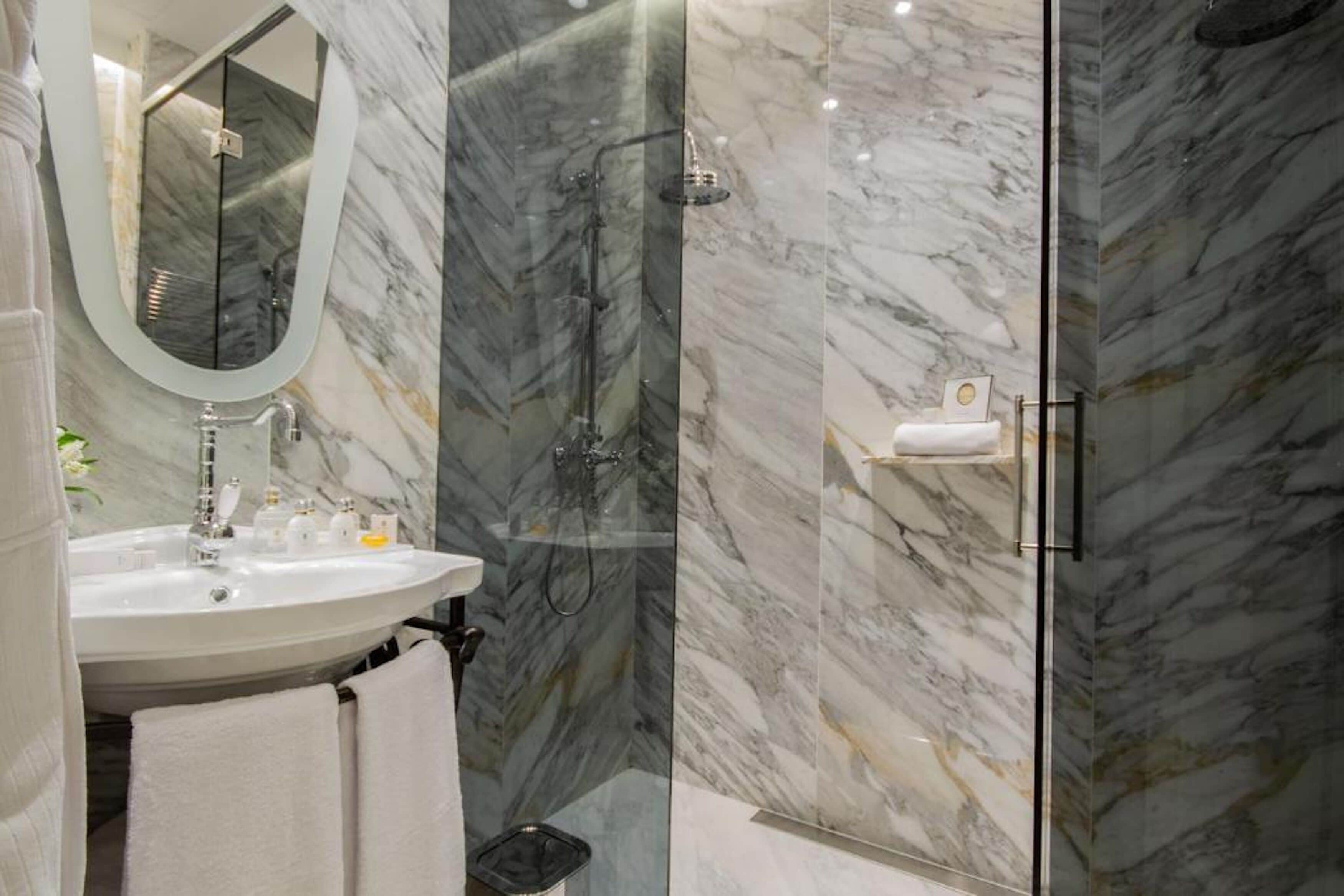 A bathroom with a marble sink, a mirror, and a glass-enclosed shower.