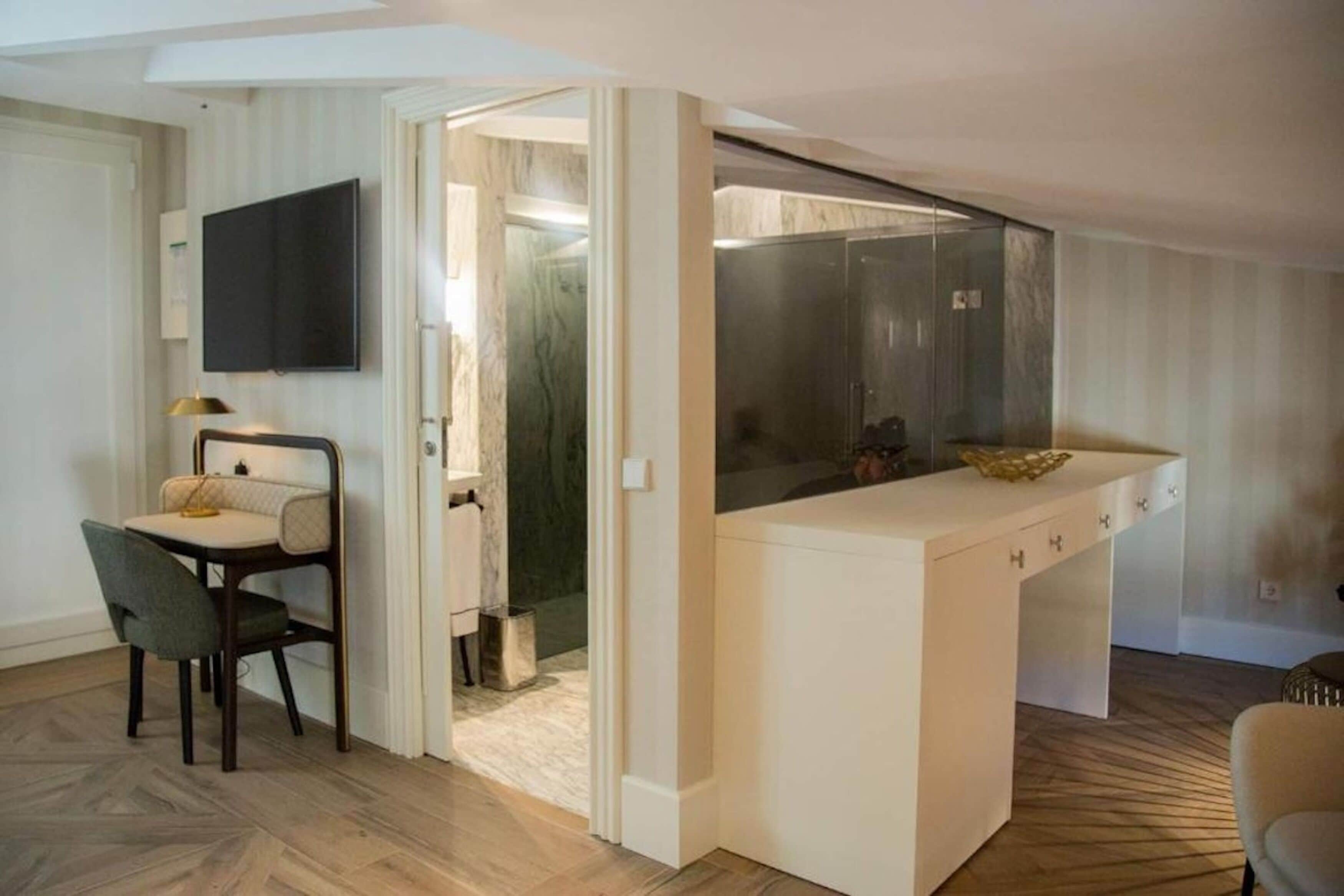 Une cuisine moderne avec un plan de travail blanc, un four encastré et une paroi en verre. On y trouve un coin repas avec une chaise et une table, ainsi qu’un téléviseur fixé au mur.