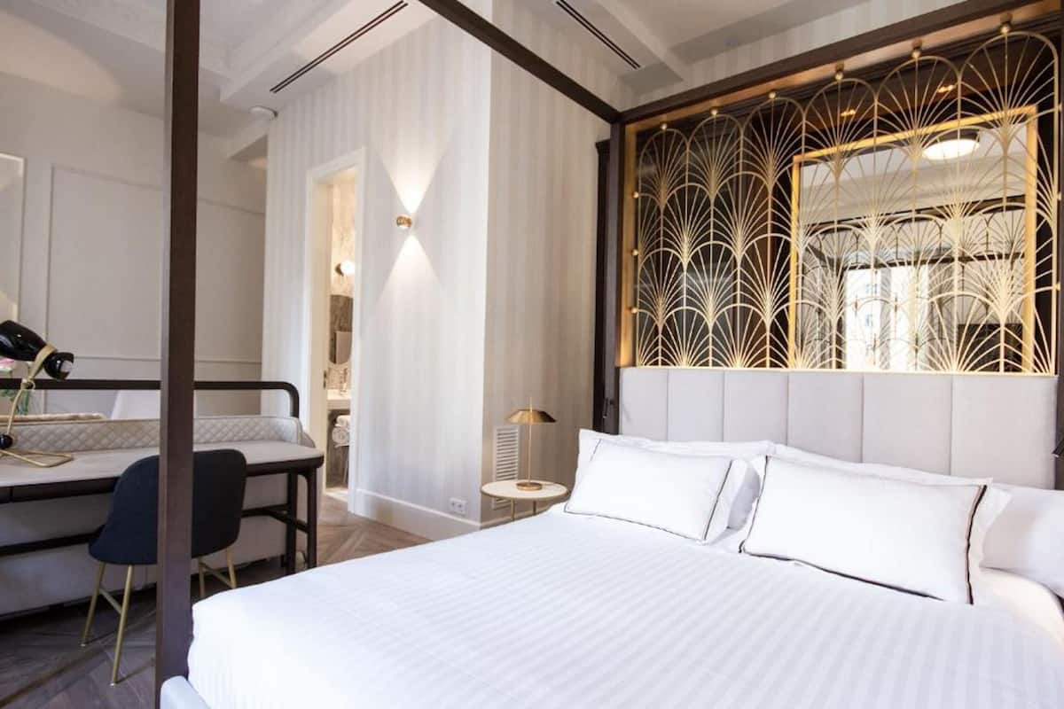 A modern hotel room with a large bed, a desk with a chair, and a decorative wall panel.